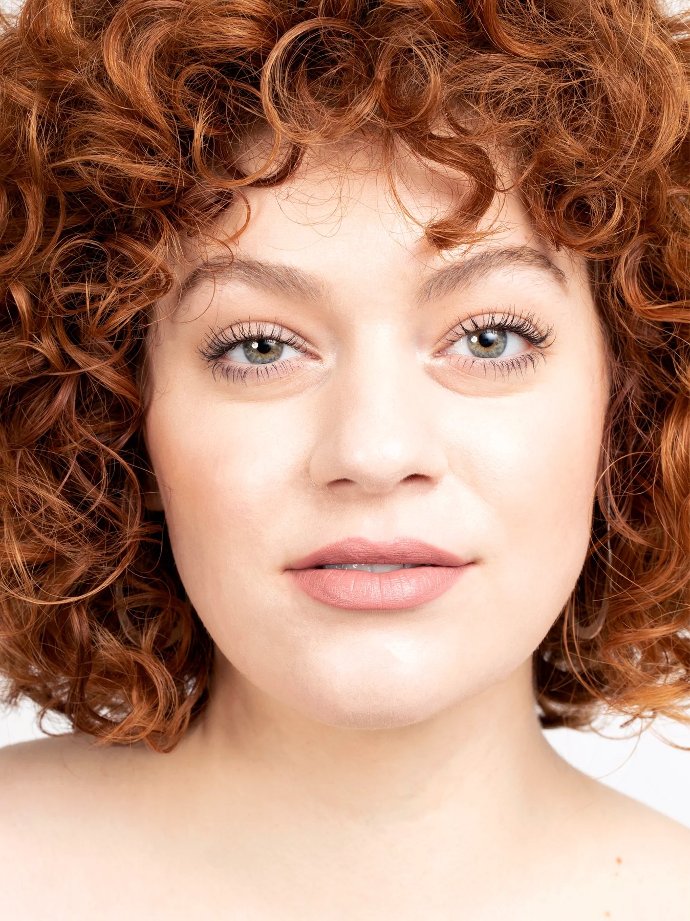 Model with curly red hair wearing soft pink lip color.