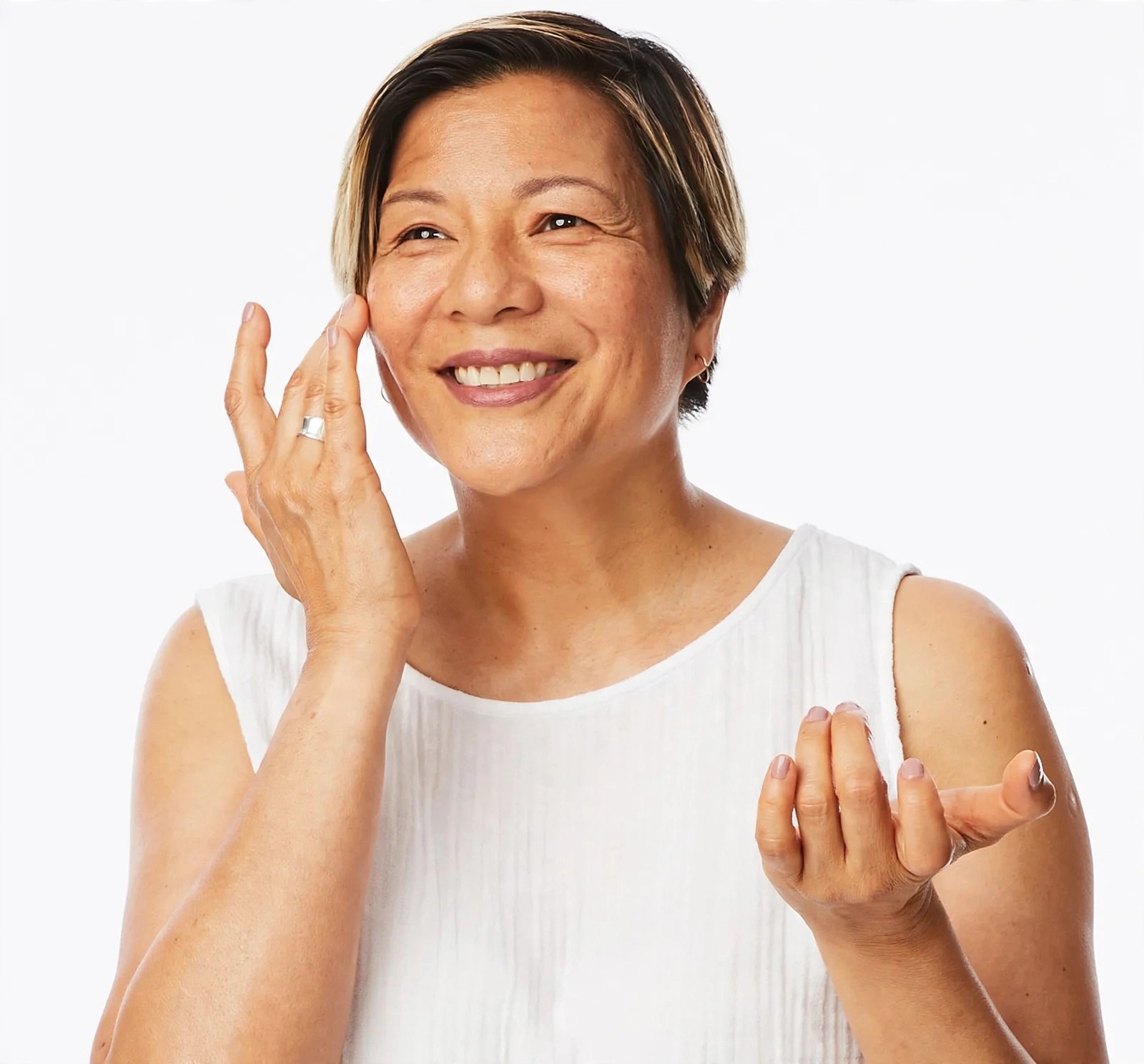 Smiling woman in white top applying cream to her cheek.