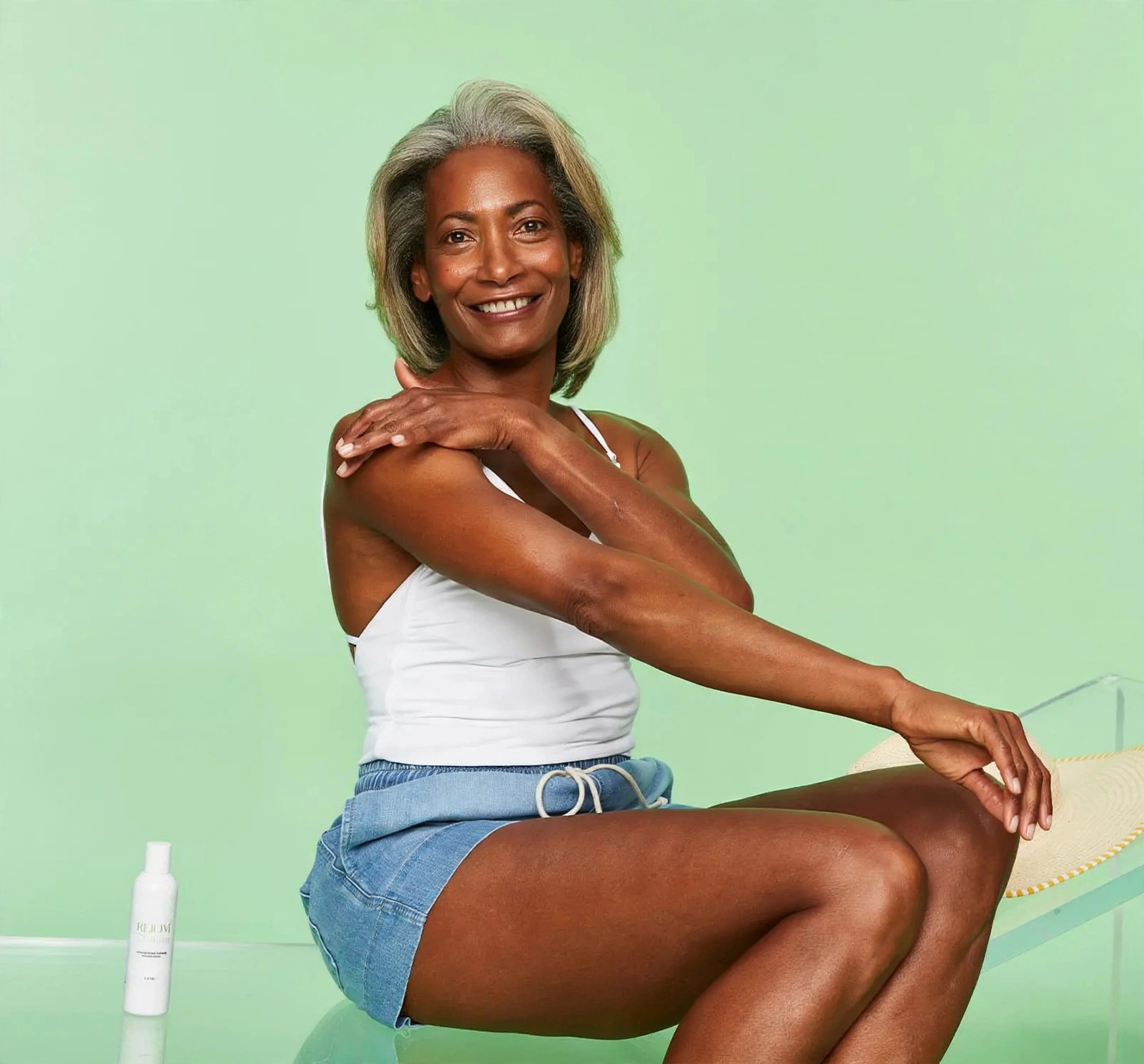 Smiling woman in denim shorts moisturizing her arm outdoors.