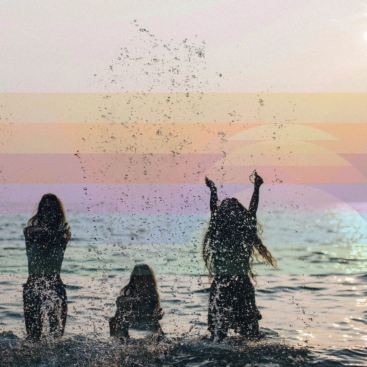 Three people splash in ocean water at sunset.
