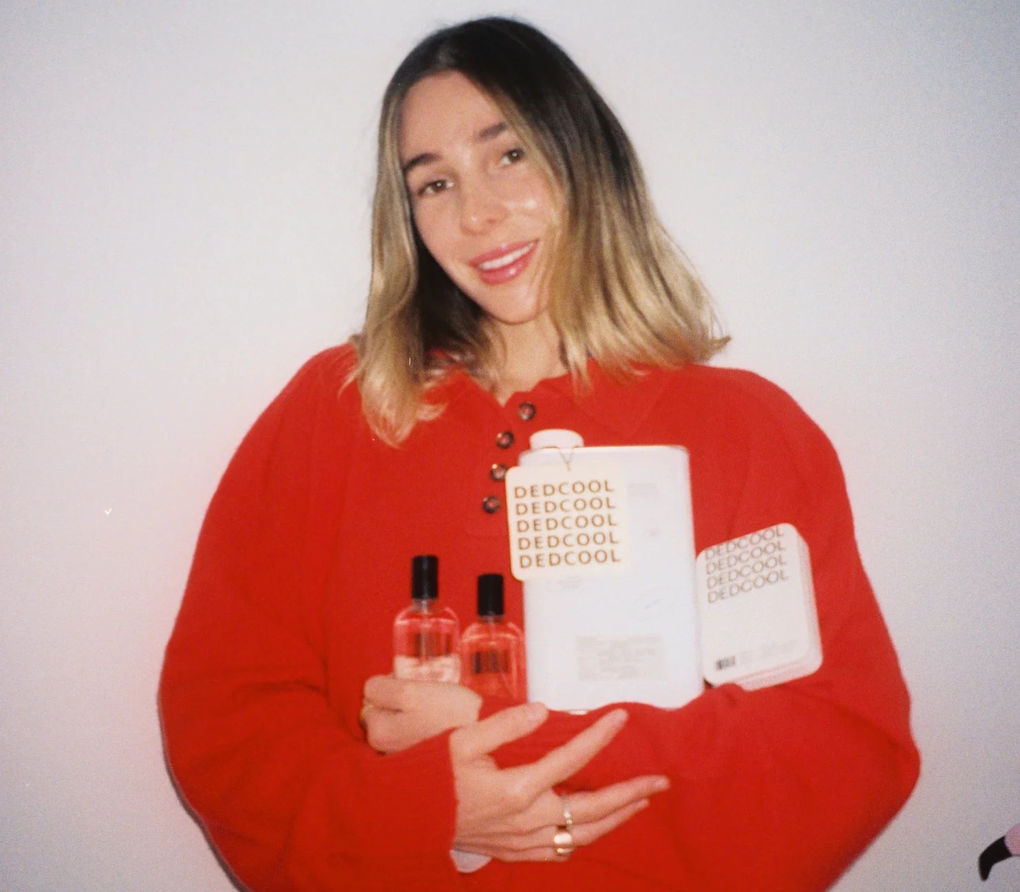 Carina Chaz in red holding two Dedcool fragrances and packaging.