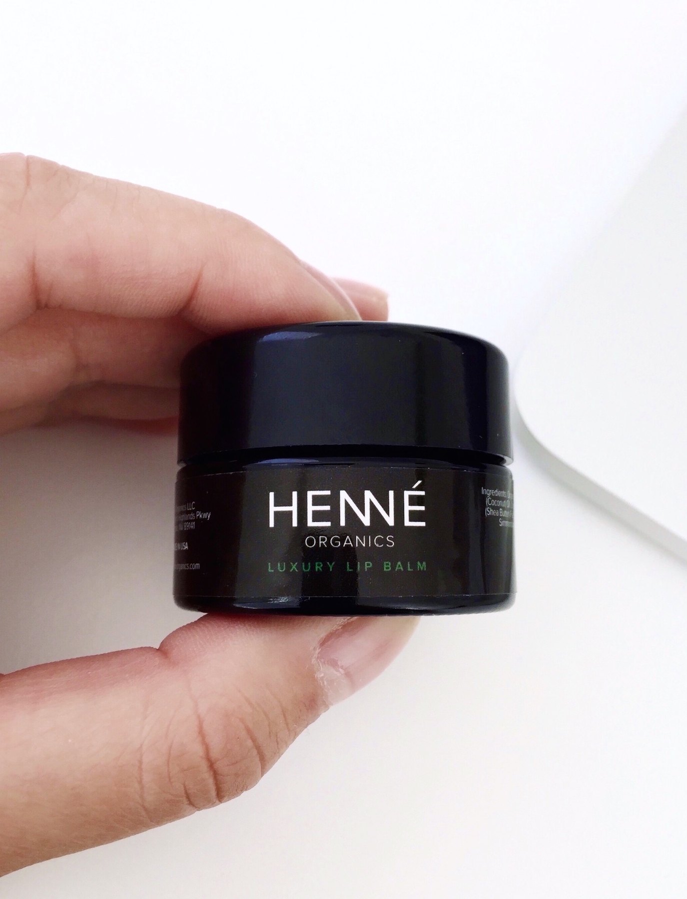 A hand holding a small black jar of Henne luxury lip balm.
