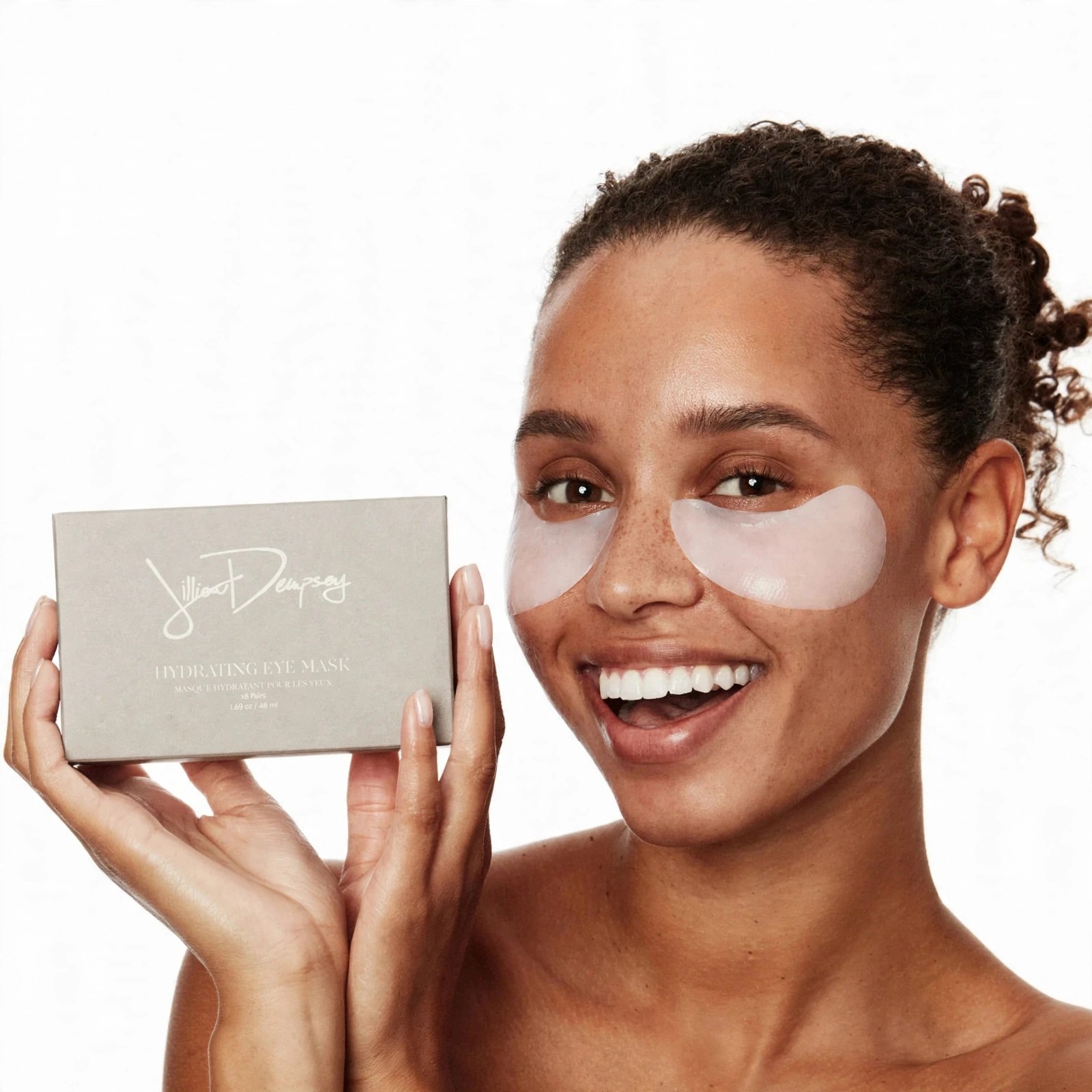 A smiling woman wears hydrating eye masks and holds the product box.