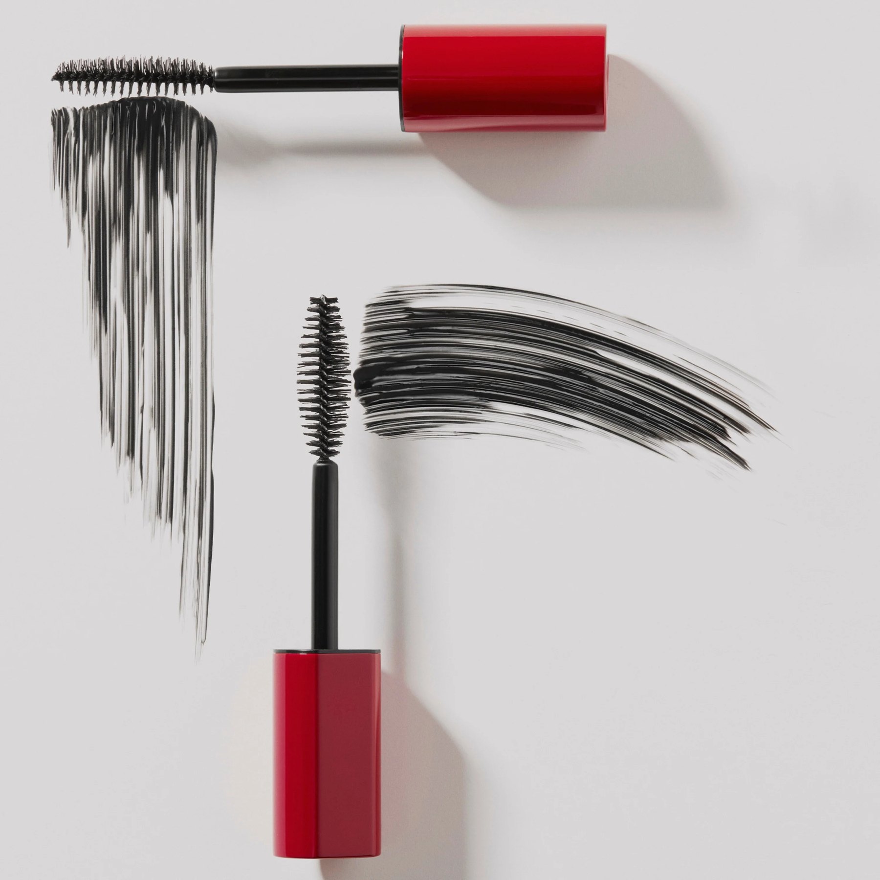Red capped mascara wands with black smears on white.