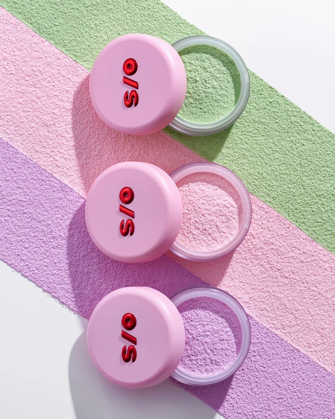 Three open pink powder jars arranged over colorful powder swatches.