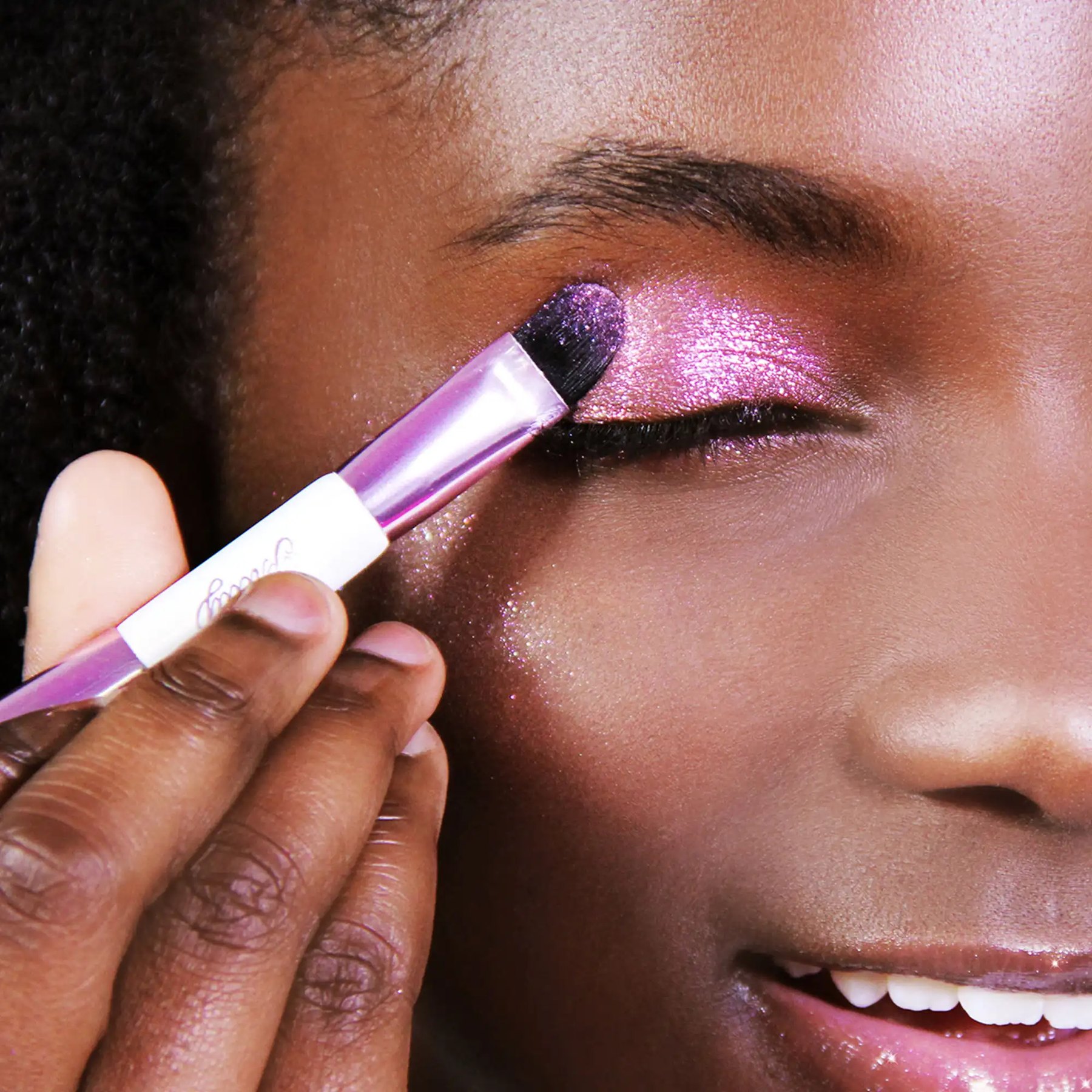 A model applies shimmery eye makeup with a small brush.