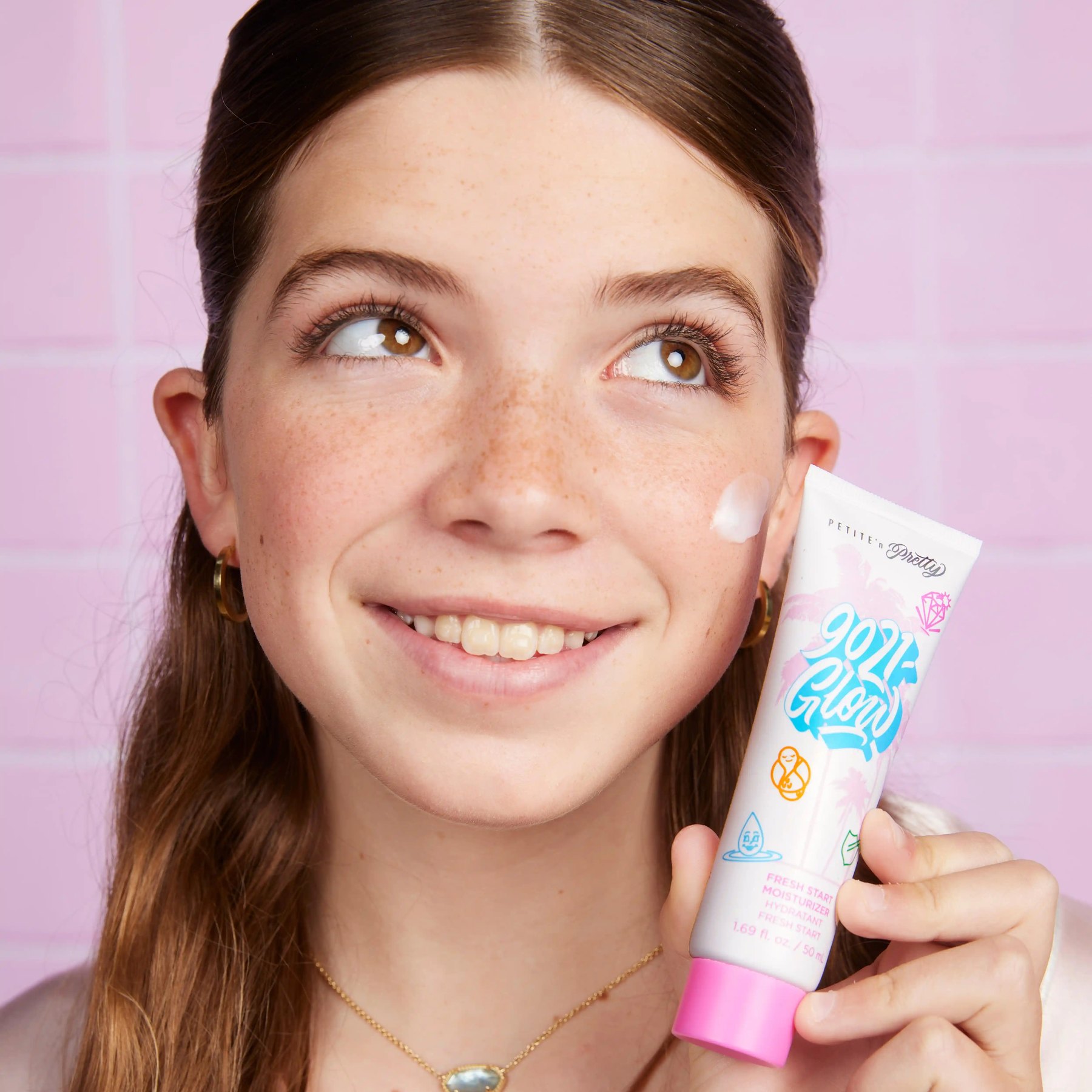 A young girl holds moisturizer beside her smiling face.