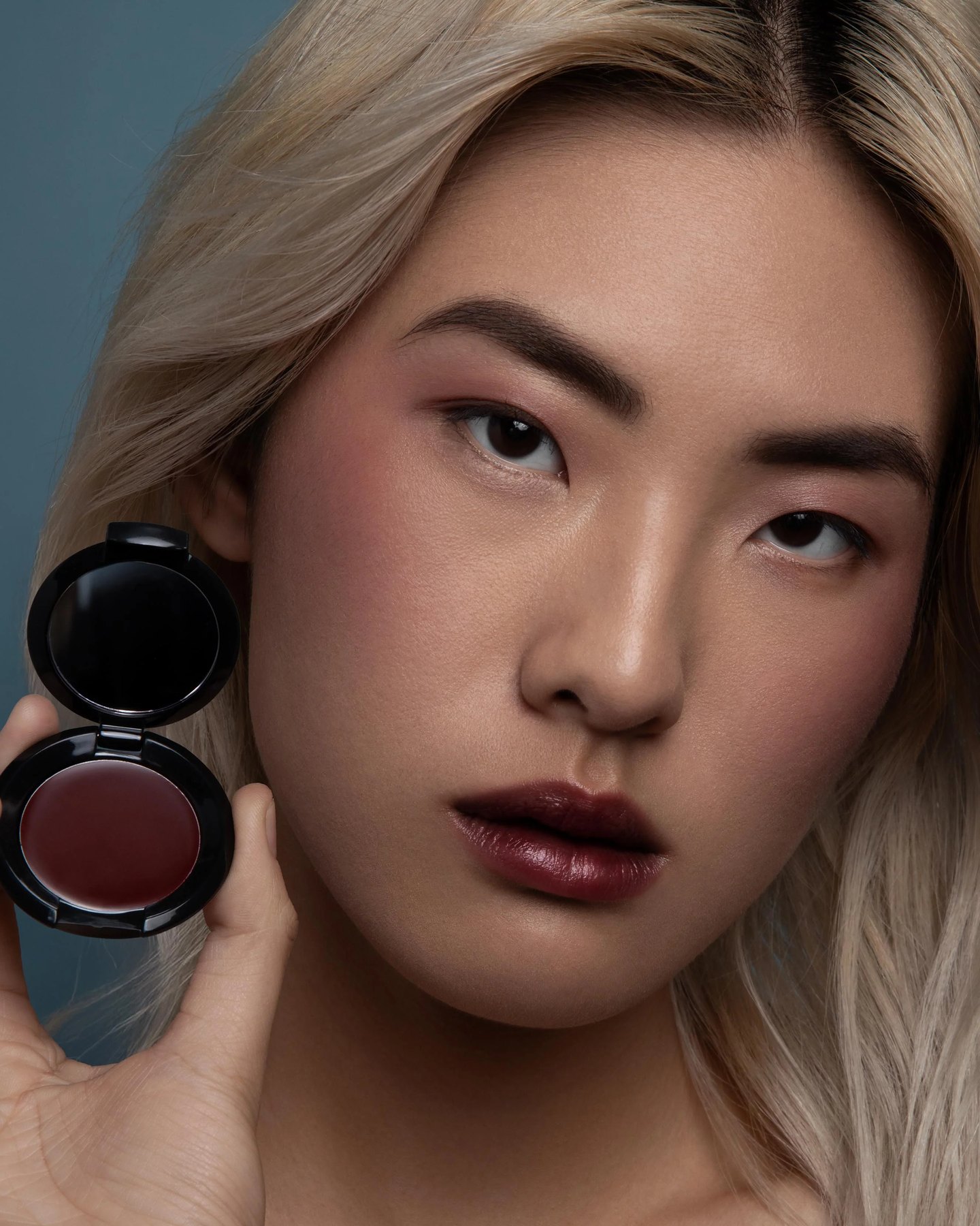 Model holding open Color Nectar Pigment Balm beside her face.