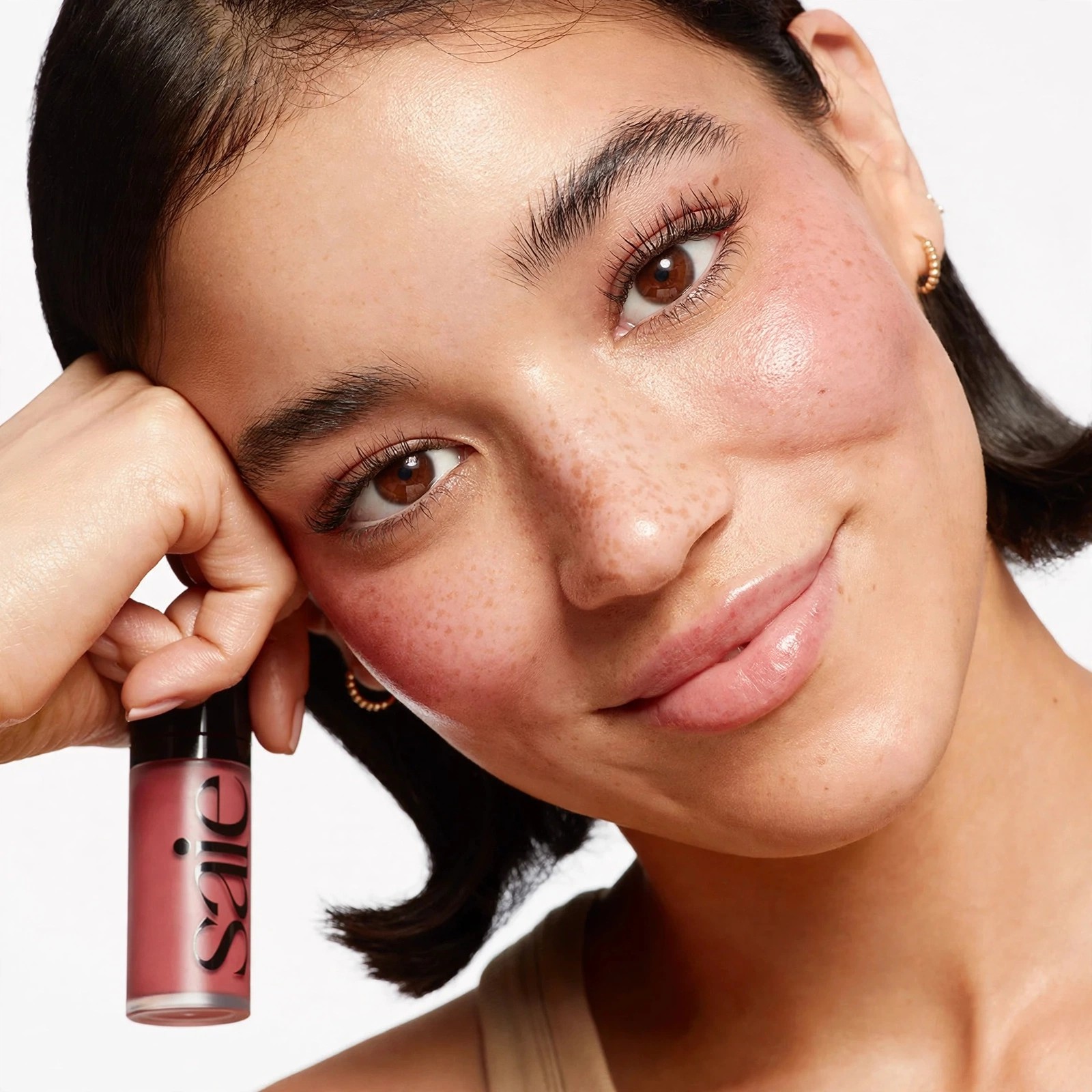 Model smiling with Dew Blush applied holding the bottle.