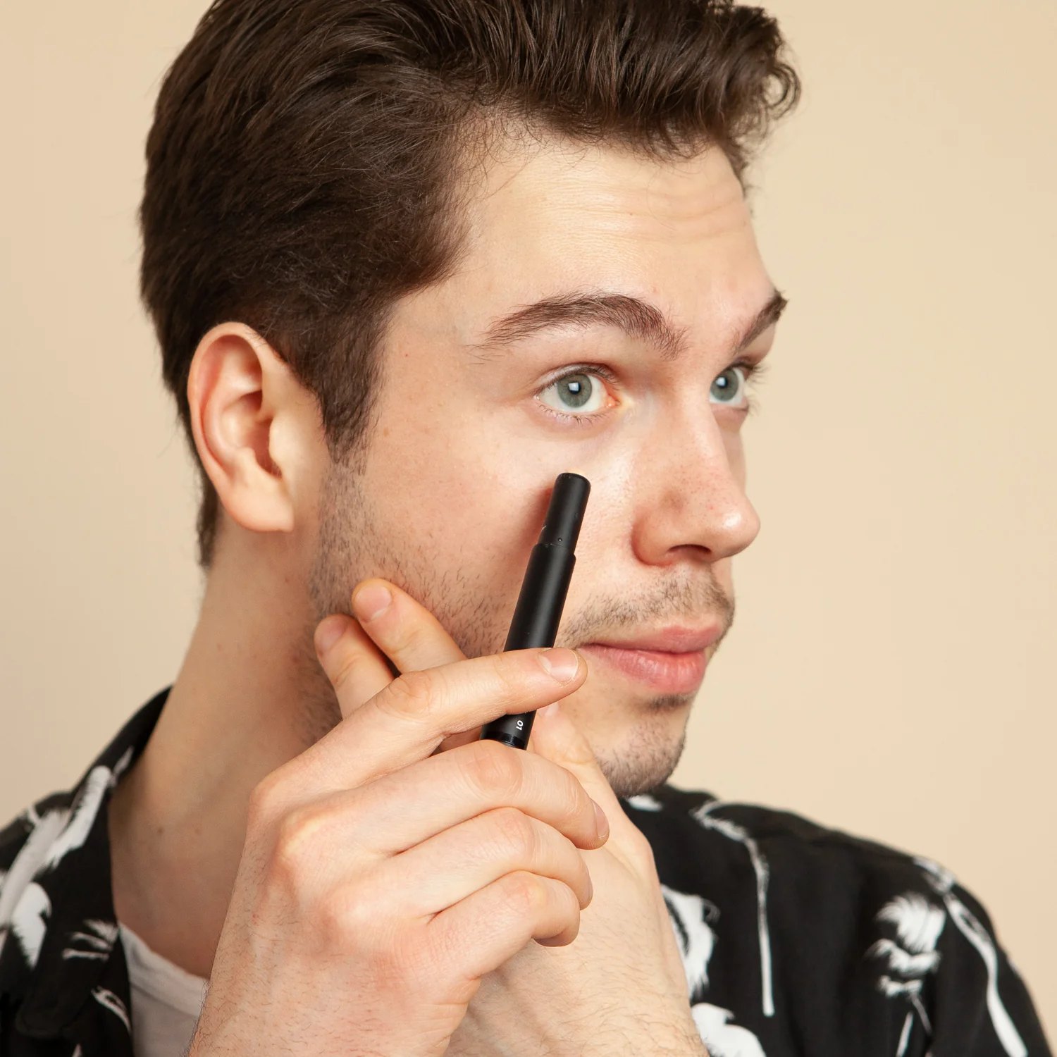 Man holds black Stryx Concealer Tool near his face.