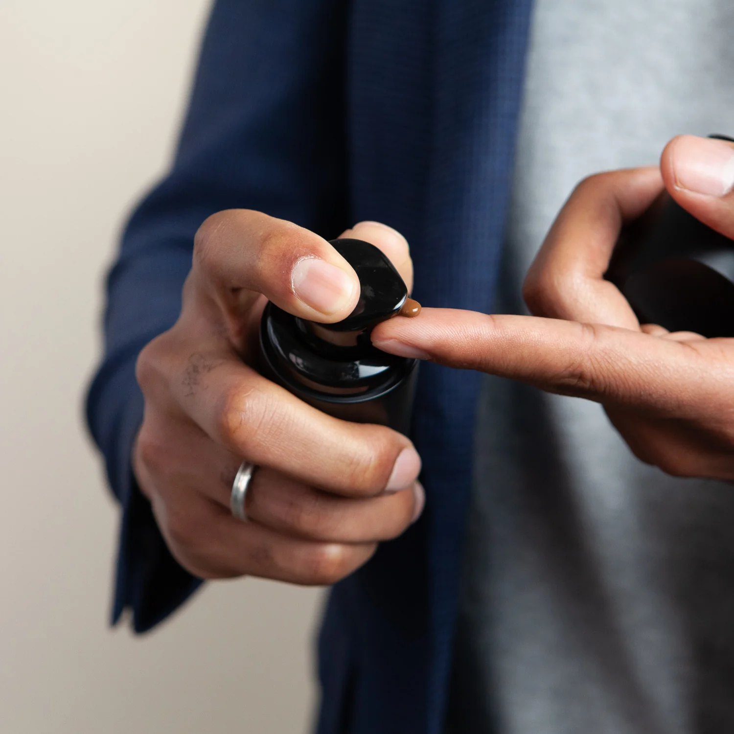 Hands dispense tinted moisturizer onto a fingertip.