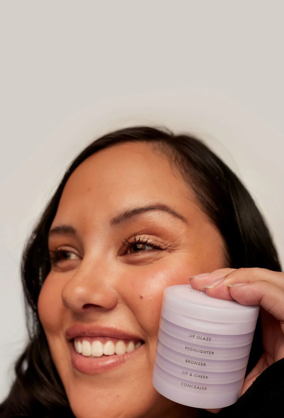 Smiling woman holding a stacked Subtl Beauty makeup compact near her face.