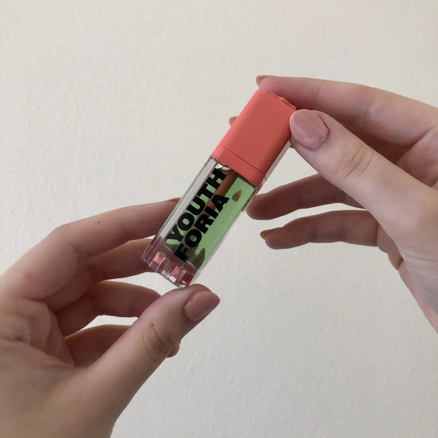 Hands holding a Youthforia green blush oil bottle.